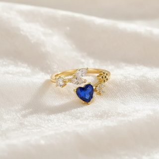 Gold ring with a blue heart-shaped gemstone on a white fabric background
