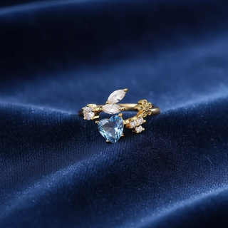 Gold ring with a heart-shaped blue gemstone on a dark blue fabric background