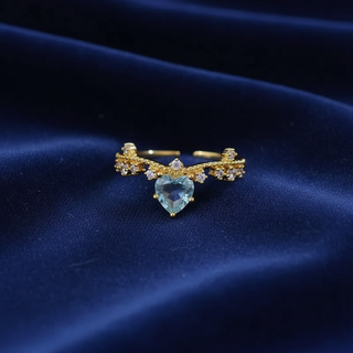 Gold ring with a heart-shaped blue gemstone on a dark blue fabric background