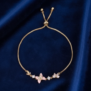 Gold bracelet with pink butterfly and clear stones on a blue fabric background
