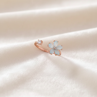Rose gold ring with a light blue flower-shaped gemstone on a soft beige background